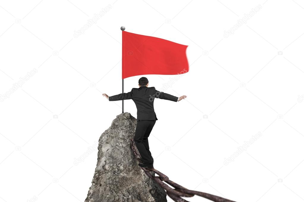 Businessman walking on rusty chain for red flag mountain top