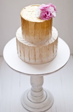 Altın ve beyaz düğün pastası ve pembe çiçekler etrafında