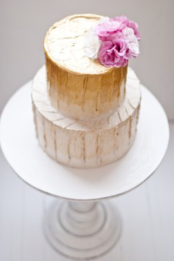 Altın ve beyaz düğün pastası ve pembe çiçekler etrafında