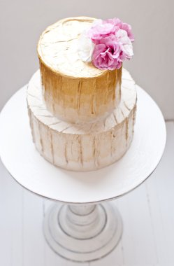 Altın ve beyaz düğün pastası ve pembe çiçekler etrafında