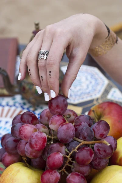 Ung kvinna håller färska druvor nära salver med äpple, päron — Stockfoto