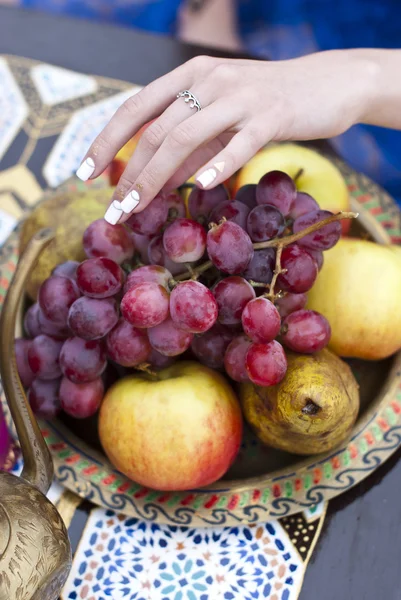 Ung kvinna håller färska druvor nära salver med äpple, päron — Stockfoto