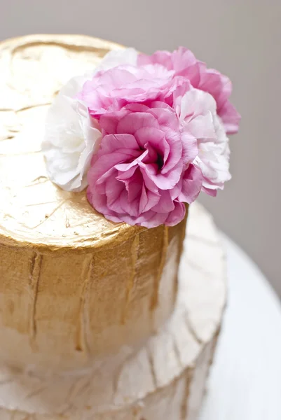 Gold and white wedding cake and pink flowers around