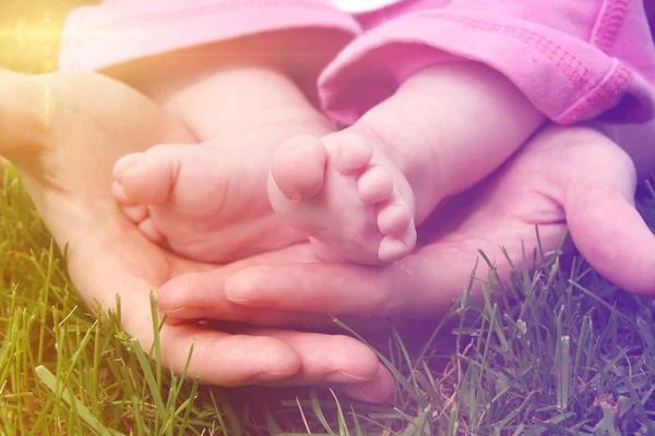 Babyfüße in den Händen der Mutter draußen im Gras — Stockfoto