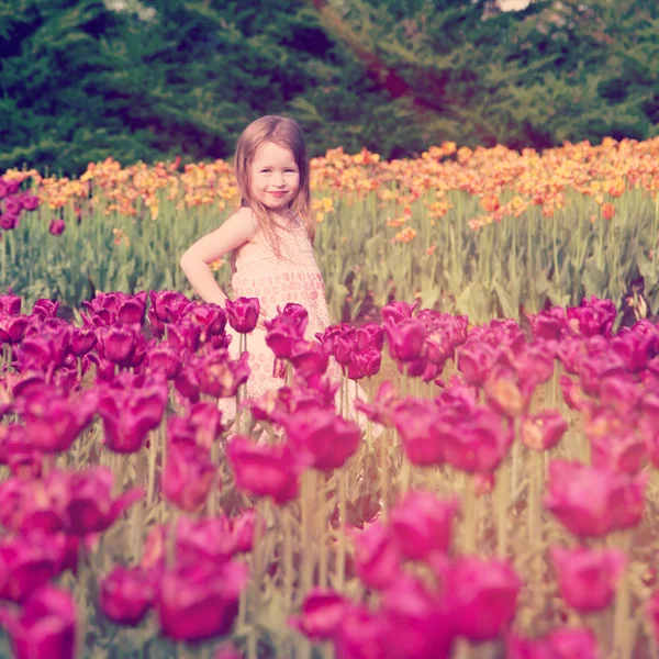 Malá holčička stojí v poli tulipánů — Stock fotografie