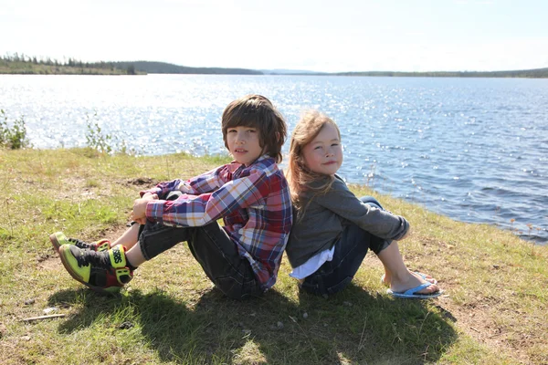 Hermano y hermana sentados cerca del lago — Foto de Stock