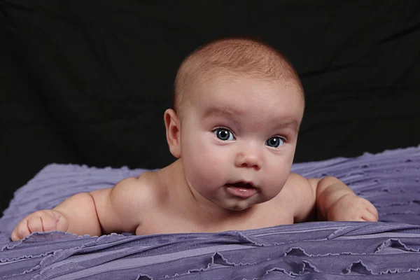 Kleines Mädchen liegt auf lila Decke — Stockfoto