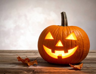 Ahşap bir yüzeye yerleştirilmiş gülümseyen bir yüzle oyulmuş Cadılar Bayramı balkabağı ve bulanık arka planda etrafa saçılmış birkaç kuru yaprak.