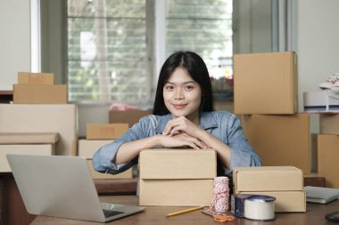 Young happy asian business woman owner of business online using laptop receive order from customer with parcel box packaging at her startup home office, online business seller and delivery clipart