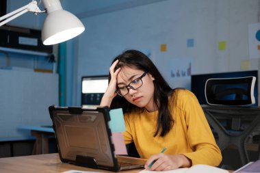 Stresli, yorgun bir kadın ofis masasında oturuyor ve fazla mesai yapıyor..