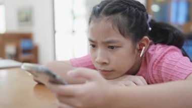 Genç kız bir masada oturuyor, kısa videolar izliyor ya da telefonuyla online oyun oynuyor. Dijital bağımlılık kavramı. Modern dünyada toplumun dijital hale getirilmesi ve bilgilendirilmesi.