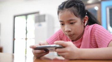 Genç kız bir masada oturuyor, kısa videolar izliyor ya da telefonuyla online oyun oynuyor. Dijital bağımlılık kavramı. Modern dünyada toplumun dijital hale getirilmesi ve bilgilendirilmesi.