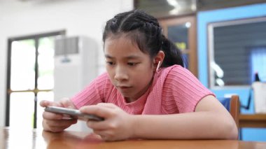 Genç kız bir masada oturuyor, kısa videolar izliyor ya da telefonuyla online oyun oynuyor. Dijital bağımlılık kavramı. Modern dünyada toplumun dijital hale getirilmesi ve bilgilendirilmesi.