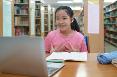 Okuldaki kütüphanede bilgisayarında video kaydı olan liseli kız. Öğretmenle internetten çalışan gülümseyen kız. Asya İlköğretim Okulu 'nun portresi kütüphanede oturmuş video görüşmesi yapıyor.