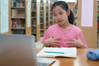 Okuldaki kütüphanede bilgisayarında video kaydı olan liseli kız. Öğretmenle internetten çalışan gülümseyen kız. Asya İlköğretim Okulu 'nun portresi kütüphanede oturmuş video görüşmesi yapıyor.