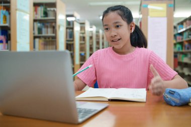 Okuldaki kütüphanede bilgisayarında video kaydı olan liseli kız. Öğretmenle internetten çalışan gülümseyen kız. Asya İlköğretim Okulu 'nun portresi kütüphanede oturmuş video görüşmesi yapıyor.