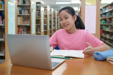 Okuldaki kütüphanede bilgisayarında video kaydı olan liseli kız. Öğretmenle internetten çalışan gülümseyen kız. Asya İlköğretim Okulu 'nun portresi kütüphanede oturmuş video görüşmesi yapıyor.