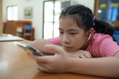 Genç kız bir masada oturuyor, kısa videolar izliyor ya da telefonuyla online oyun oynuyor. Dijital bağımlılık kavramı. Modern dünyada toplumun dijital hale getirilmesi ve bilgilendirilmesi.