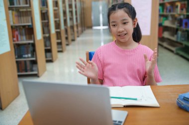 Okuldaki kütüphanede bilgisayarında video kaydı olan liseli kız. Öğretmenle internetten çalışan gülümseyen kız. Asya İlköğretim Okulu 'nun portresi kütüphanede oturmuş video görüşmesi yapıyor.