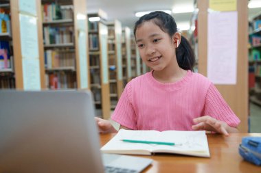 Okuldaki kütüphanede bilgisayarında video kaydı olan liseli kız. Öğretmenle internetten çalışan gülümseyen kız. Asya İlköğretim Okulu 'nun portresi kütüphanede oturmuş video görüşmesi yapıyor.