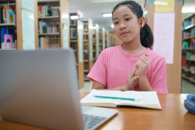 Okuldaki kütüphanede bilgisayarında video kaydı olan liseli kız. Öğretmenle internetten çalışan gülümseyen kız. Asya İlköğretim Okulu 'nun portresi kütüphanede oturmuş video görüşmesi yapıyor.