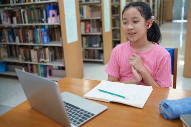 Okuldaki kütüphanede bilgisayarında video kaydı olan liseli kız. Öğretmenle internetten çalışan gülümseyen kız. Asya İlköğretim Okulu 'nun portresi kütüphanede oturmuş video görüşmesi yapıyor.