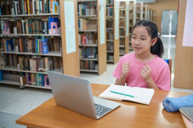 Okuldaki kütüphanede bilgisayarında video kaydı olan liseli kız. Öğretmenle internetten çalışan gülümseyen kız. Asya İlköğretim Okulu 'nun portresi kütüphanede oturmuş video görüşmesi yapıyor.