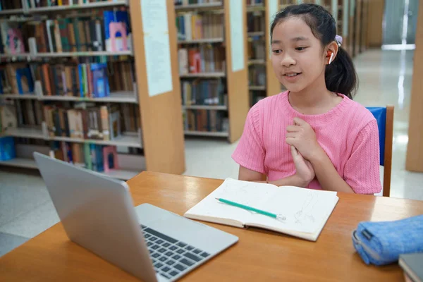 Okuldaki kütüphanede bilgisayarında video kaydı olan liseli kız. Öğretmenle internetten çalışan gülümseyen kız. Asya İlköğretim Okulu 'nun portresi kütüphanede oturmuş video görüşmesi yapıyor.