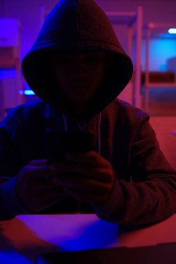 Karanlık bir odada bilgisayar üzerinde çalışan kapüşonlu bir bilgisayar korsanı. Siber güvenlik, hackleme, siber suç ve veri gizliliği tehditleri için bir kavram.