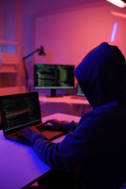 Karanlık bir odada bilgisayar üzerinde çalışan kapüşonlu bir bilgisayar korsanı. Siber güvenlik, hackleme, siber suç ve veri gizliliği tehditleri için bir kavram.