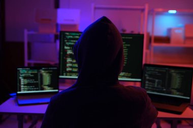 Karanlık bir odada bilgisayar üzerinde çalışan kapüşonlu bir bilgisayar korsanı. Siber güvenlik, hackleme, siber suç ve veri gizliliği tehditleri için bir kavram.
