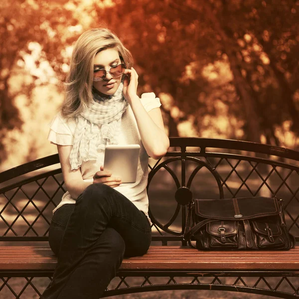 Young fashion woman using digital tablet computer in city park Stylish female model in sunglasses and white t-shirt