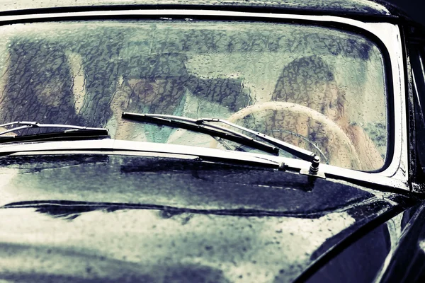 Young people driving retro car in the rain