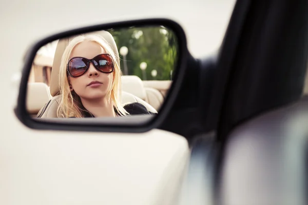 Blond fashion woman in sunglasses looking in the car rear view m