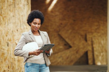 Afrikalı bir kadın mimarın dijital tablet kullanarak ve yeni ahşap bir evin şantiyesini kontrol ederken çekilmiş..