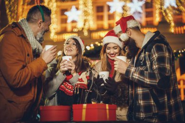 Bir grup neşeli genç arkadaşın birlikte eğlendiği ve bir akşam partisinde Noel pazarında sıcak şarabın tadını çıkardığı bir fotoğraf..