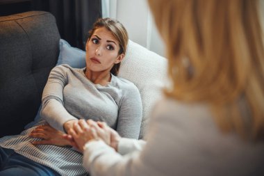 Endişeli genç bir kadının kadın psikoterapistiyle oturma odasındaki bir kanepede otururken tartıştığı görüntüler..