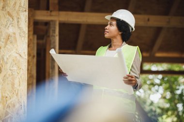 Yeni ahşap bir evin inşaat alanındaki planları kontrol eden Afrikalı bir kadın mimar vuruldu. Koruyucu iş kıyafeti ve beyaz kask giyiyor..