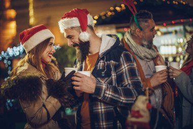 Güzel bir çiftin birlikte eğlendiği ve akşam partisinde Noel pazarında sıcak şarabın tadını çıkardığı bir fotoğraf..