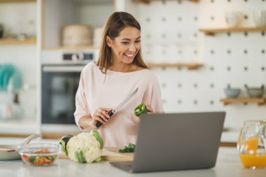 Genç bir kadının evde sağlıklı bir yemek hazırlarken bilgisayarı kullanarak video bloğu hazırlaması..