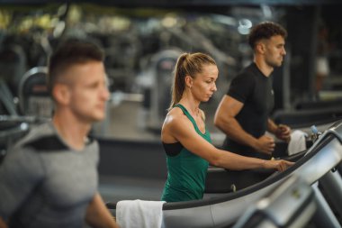 Spor salonundaki koşu bandında egzersiz yapan üç gencin fotoğrafı..