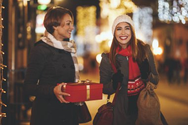 Neşeli iki genç kadın Noel gecesi şehir sokağında eğleniyorlar. Gülüyor ve tatil için hediyeler alıyorlar..
