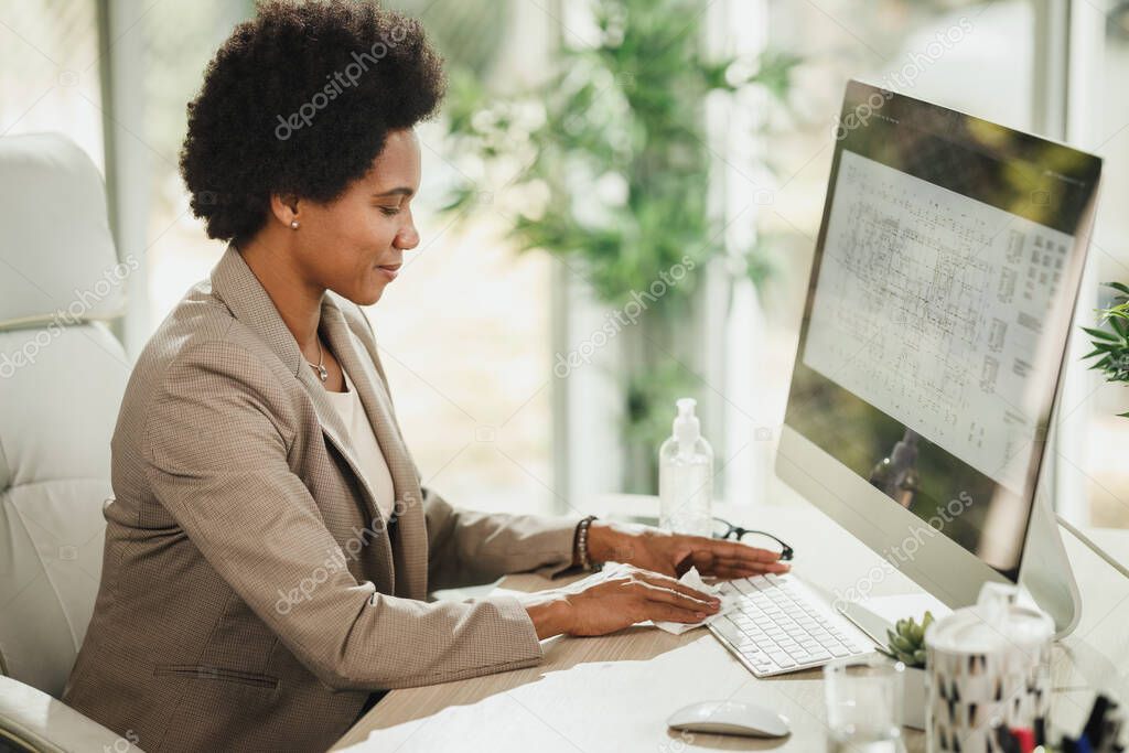 Shot of an attractive African businesswoman sitting alone in her office and using antiseptic gel to disinfect computer keyboard during COVID-19 pandemic.