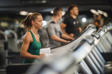 Spor salonunda koşu bandında koşan genç bir kadının fotoğrafı..