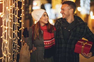 Neşeli genç bir çiftin çekimi Noel gecesi şehir sokağında eğleniyor. Gülüyor ve tatil için hediyeler alıyorlar..