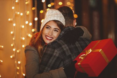 Neşeli genç bir çiftin çekimi Noel gecesi şehir sokağında eğleniyor. Birbirlerine sarılıp bayram hediyeleri veriyorlar..