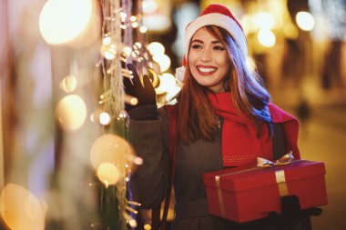 Kırmızı hediye kutusu olan mutlu genç bir kadının çekimi Noel zamanı şehir sokaklarında eğleniyor..