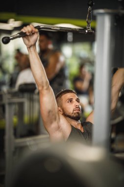 Spor giyim bölümünde spor salonunda çalışan kaslı bir adamı vurmuşlar. Sırt kaslarını ağırlıkla şişiriyor..