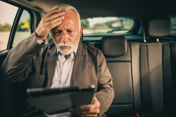 彼の朝の通勤中に車の後部座席に座っている間 デジタルタブレットを使用して心配している上級ビジネスマンのショット — ストック写真