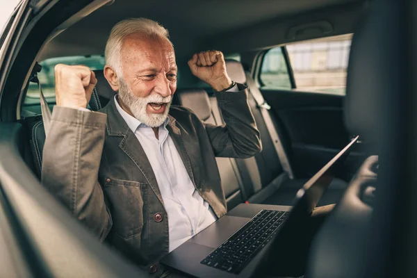 通勤中に車の後部座席に座って成功した仕事を祝うためにノートパソコンを使用して陽気な先輩のショット — ストック写真